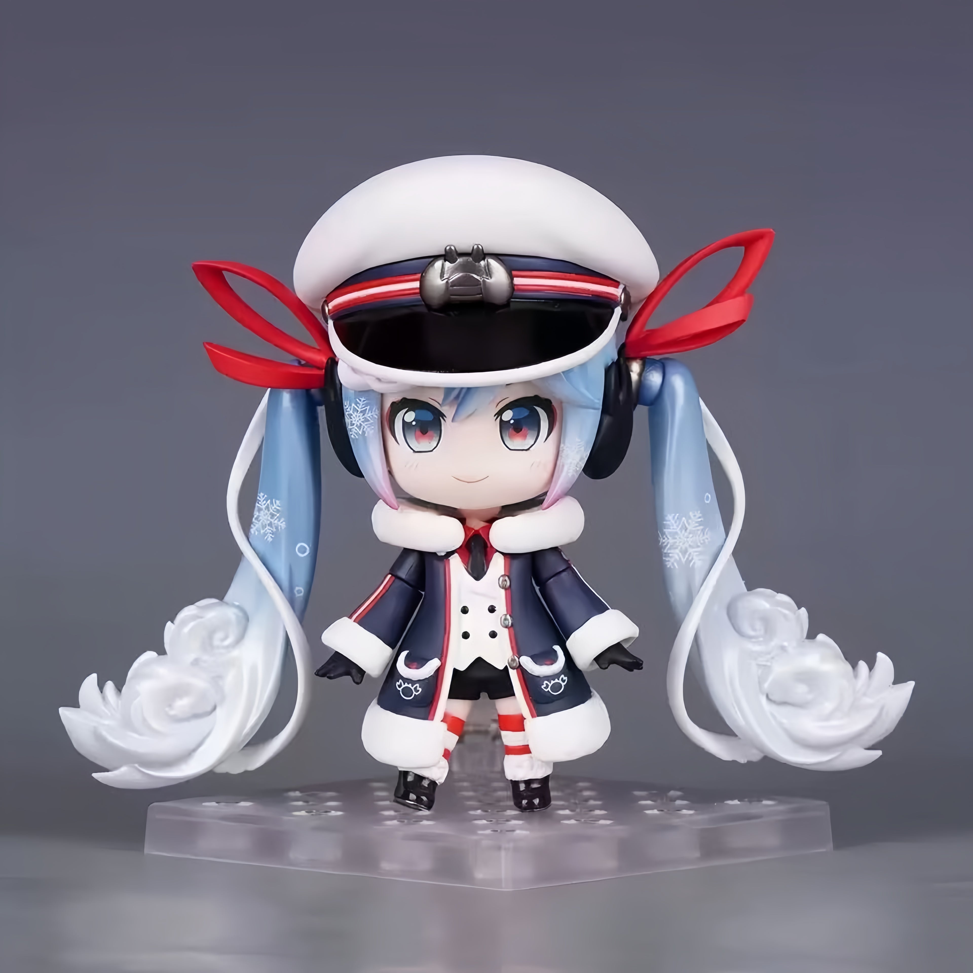 Snow Miku VOCALOID chibi action figure with twin-tail hairstyle, white blue red and navy winter outfit, snow-inspired details, and clear display base.